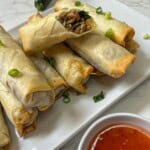 A plate of spring rolls with sauce and green onions.