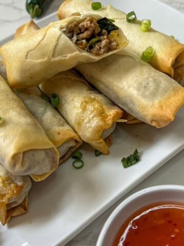 A plate of spring rolls with sauce and green onions.