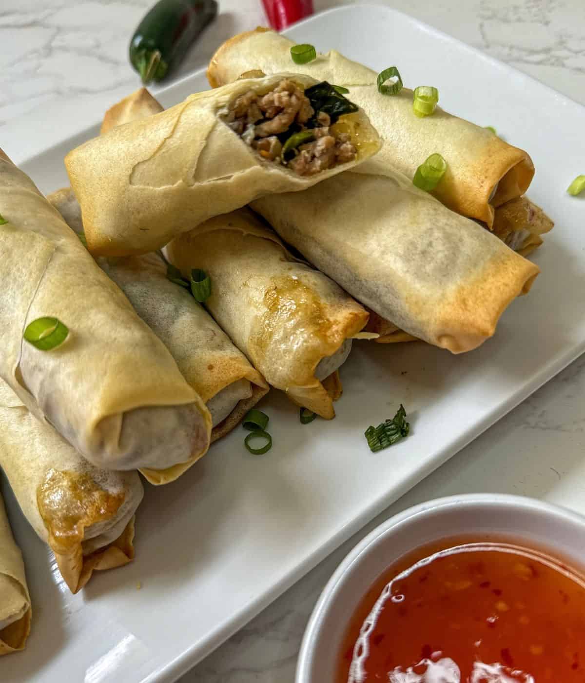 A plate of spring rolls with sauce and dipping sauce.