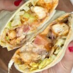 A person holding up a wrap with chicken and lettuce.