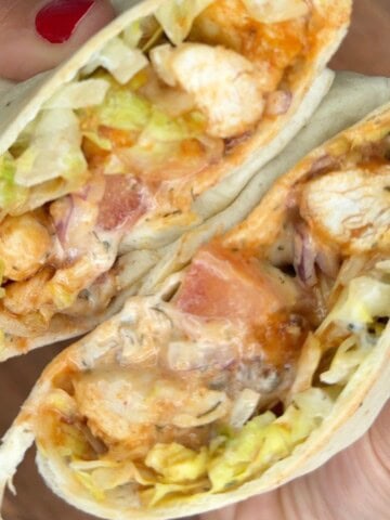 A person holding up a wrap with chicken and lettuce.