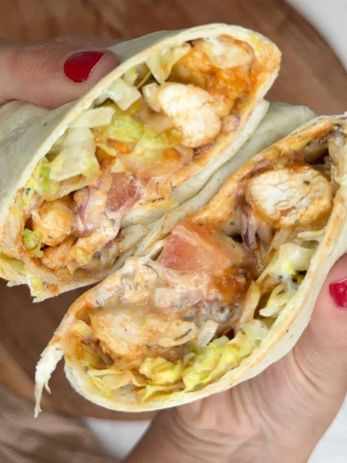 A person holding up a chicken wrap with cheese and lettuce.