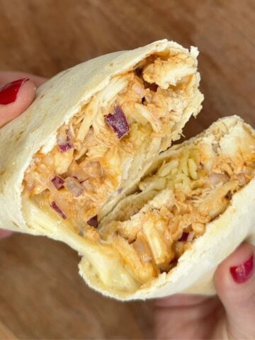 Someone holding a cut open wrap with chicken onion and cheese inside.