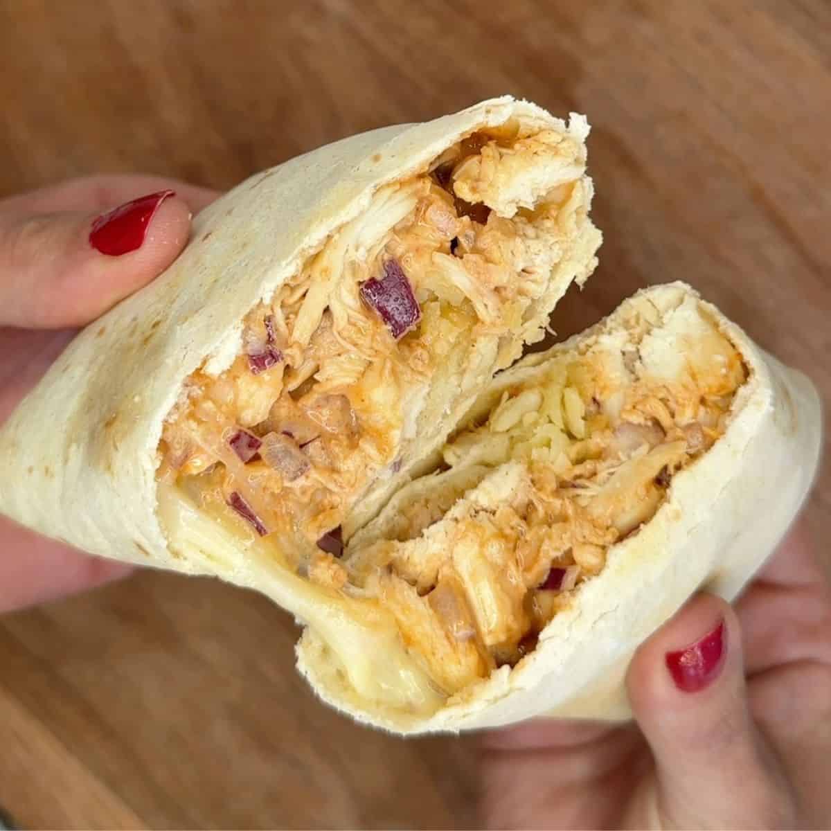 Someone holding a cut open wrap with chicken onion and cheese inside.