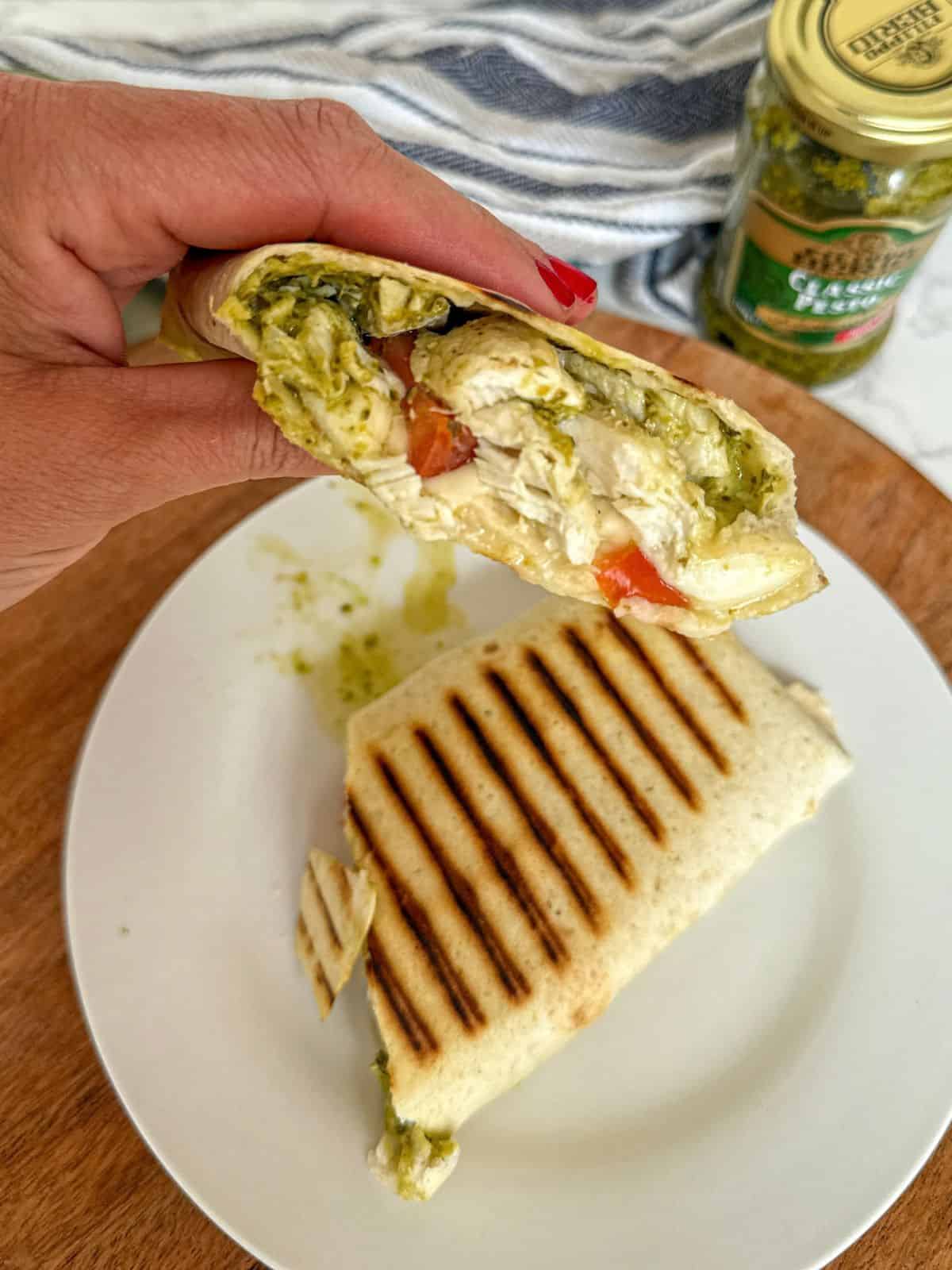 Someone holding half a chicken pesto and mozzarella wrap. The other half is on a white plate.