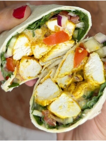 Someone holding a open chicken tikka wrap cut in half.