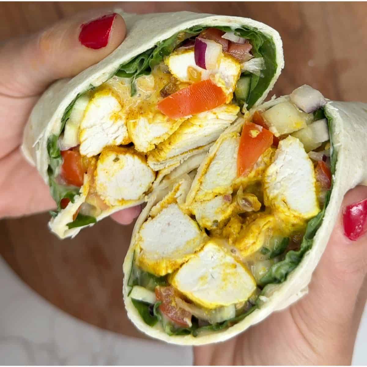 Someone holding a open chicken tikka wrap cut in half.