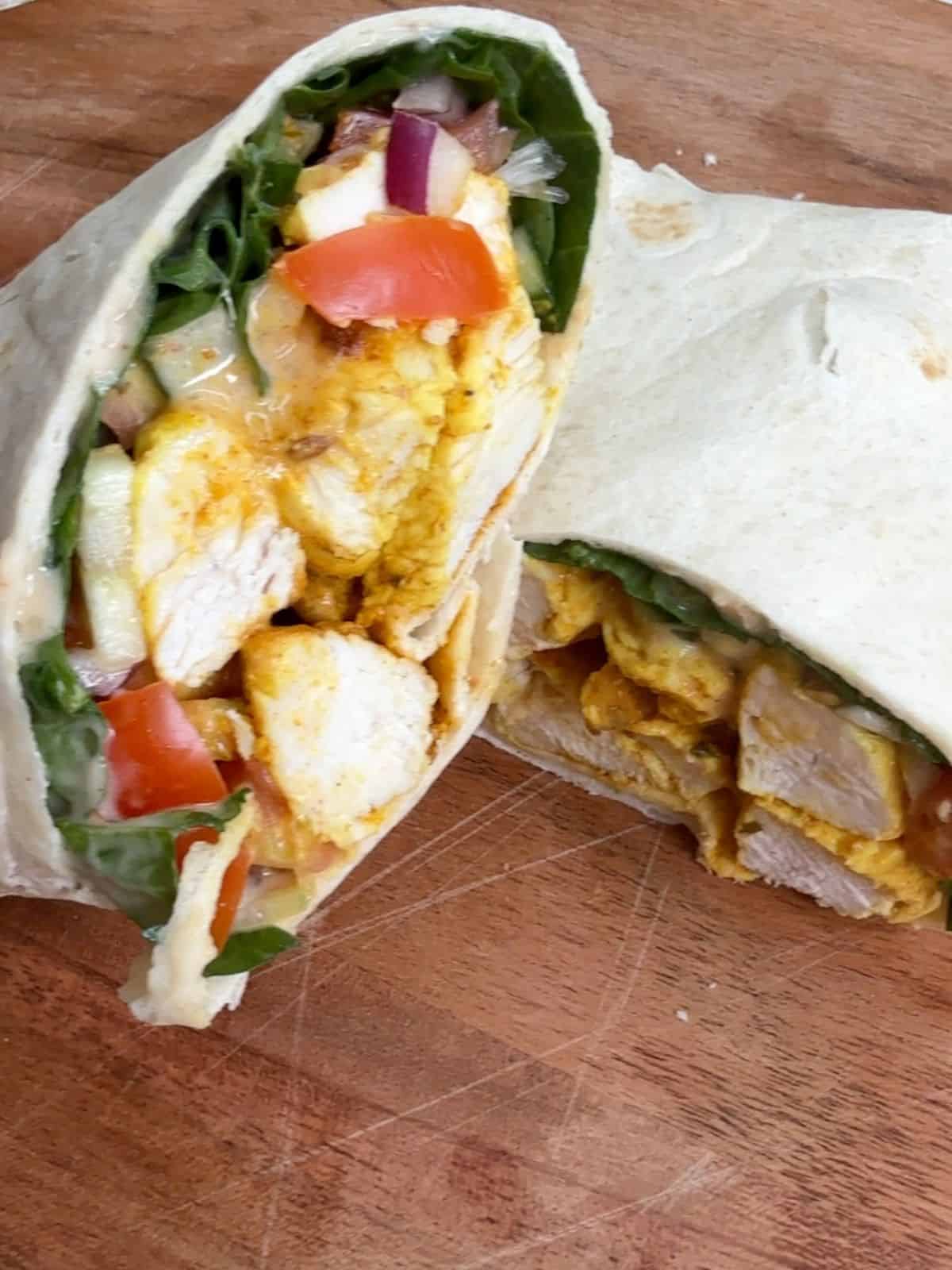 A chicken tikka wrap cut in half on a chopping board.