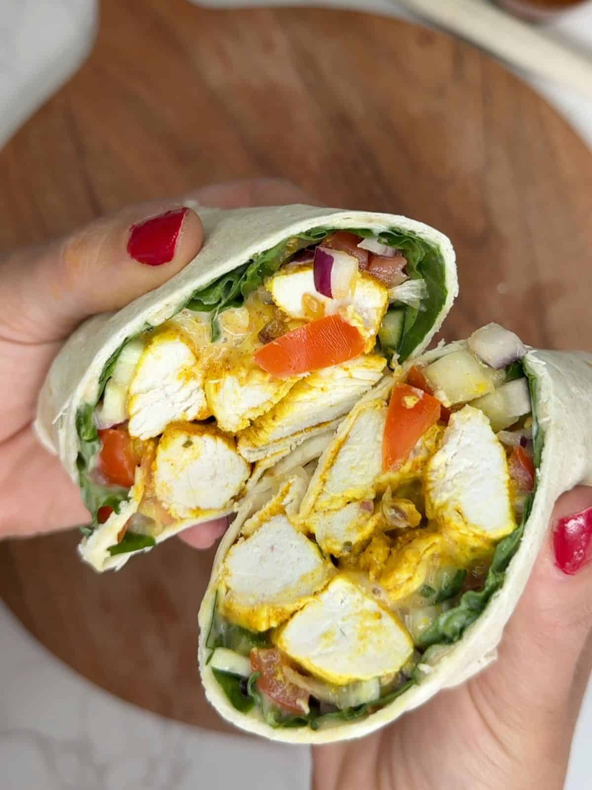 Someone holding a open chicken tikka wrap cut in half.