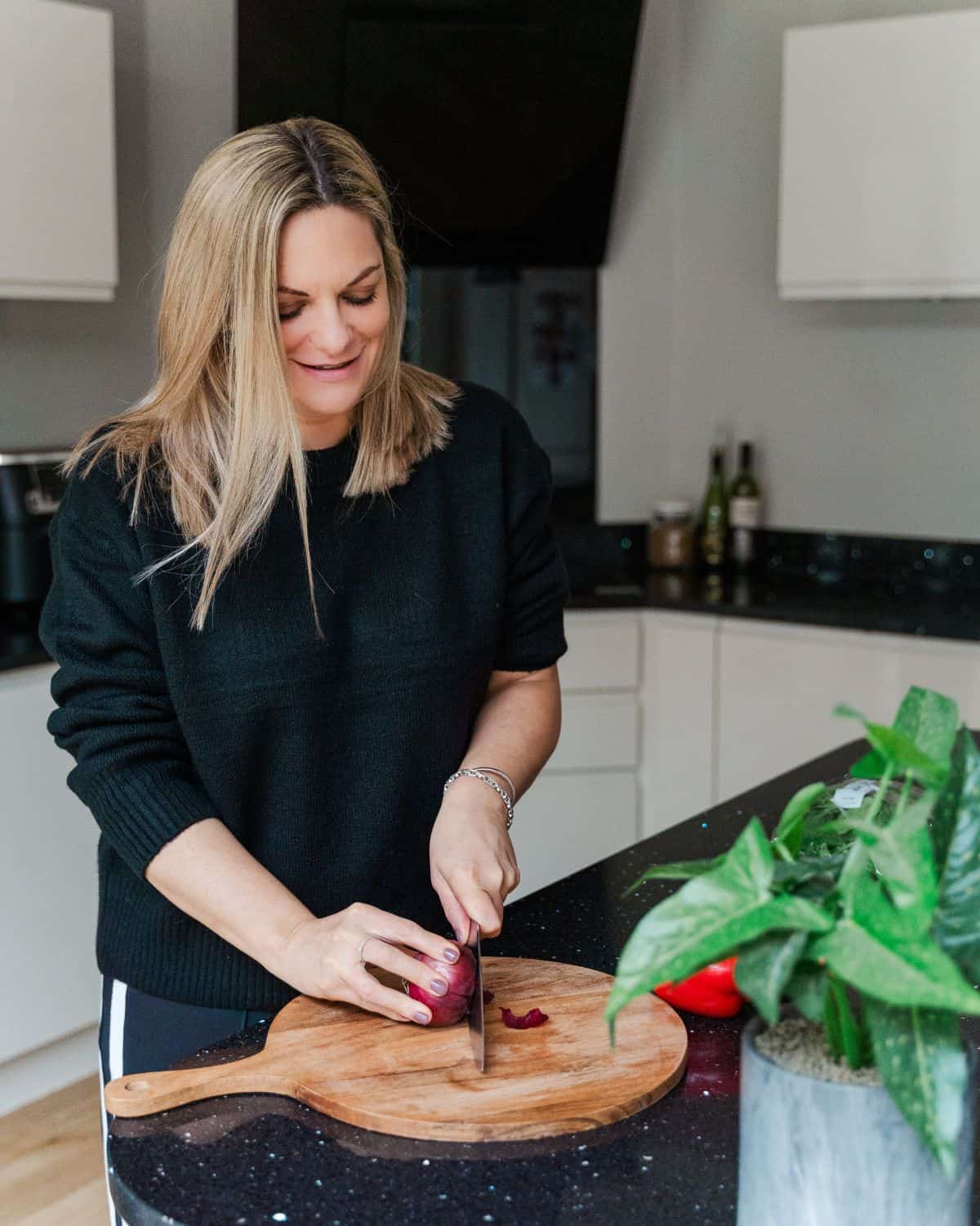 A lady chopping a red onion on a chopping board.