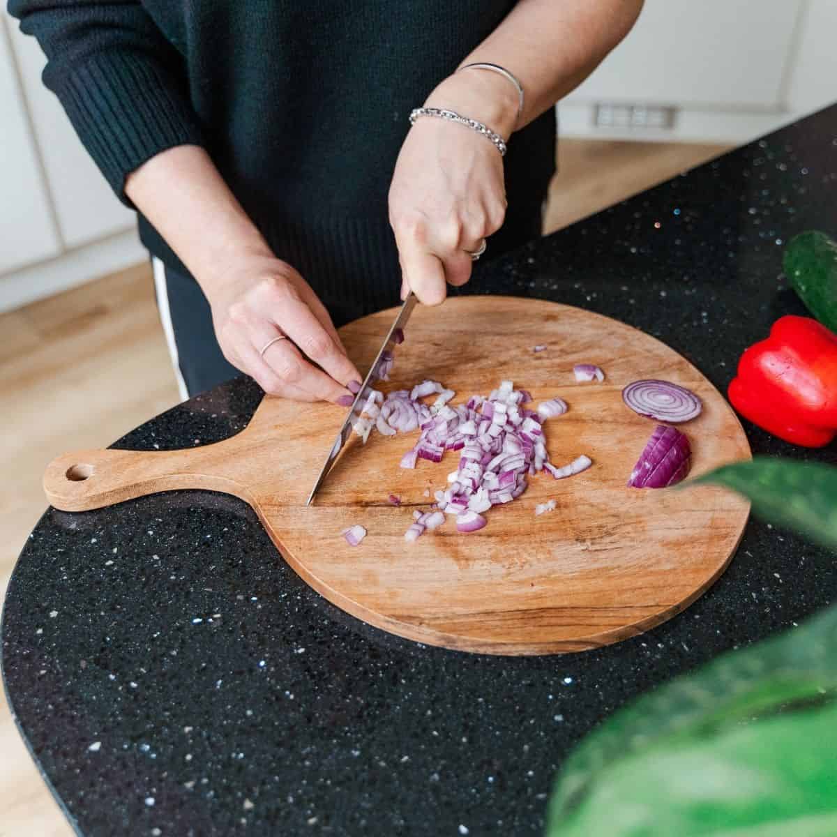 Someone dicing red onion on a wooden chopping board.