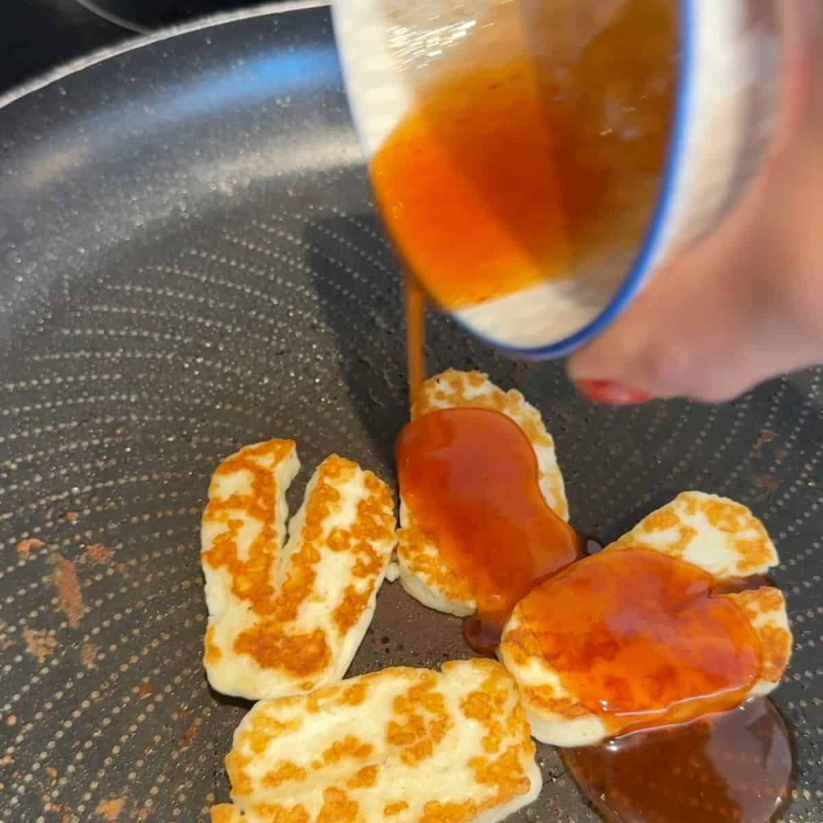Hot honey being poured over halloumi in a pan.