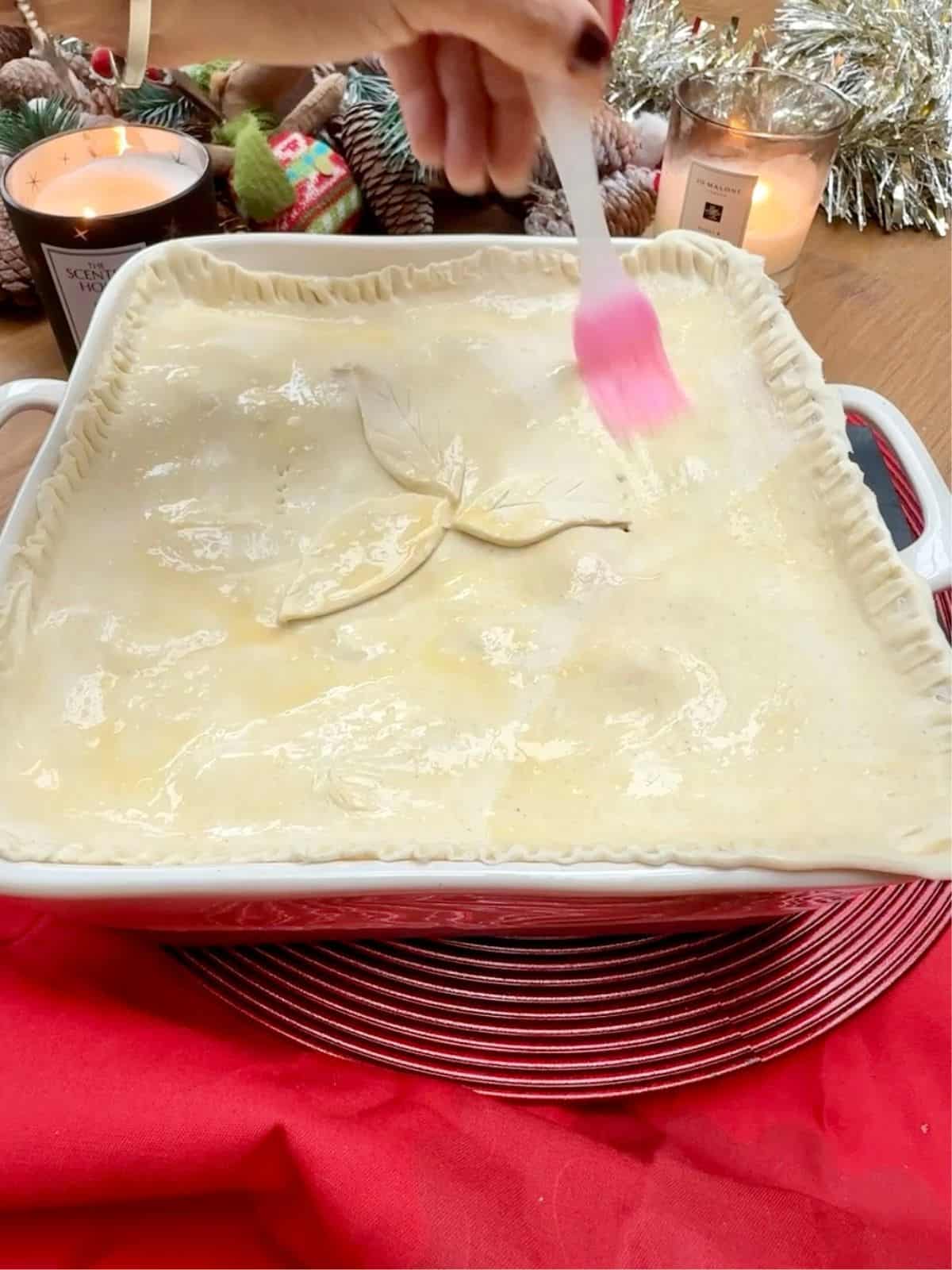 A puff pastry pie top being brushed with egg wash.