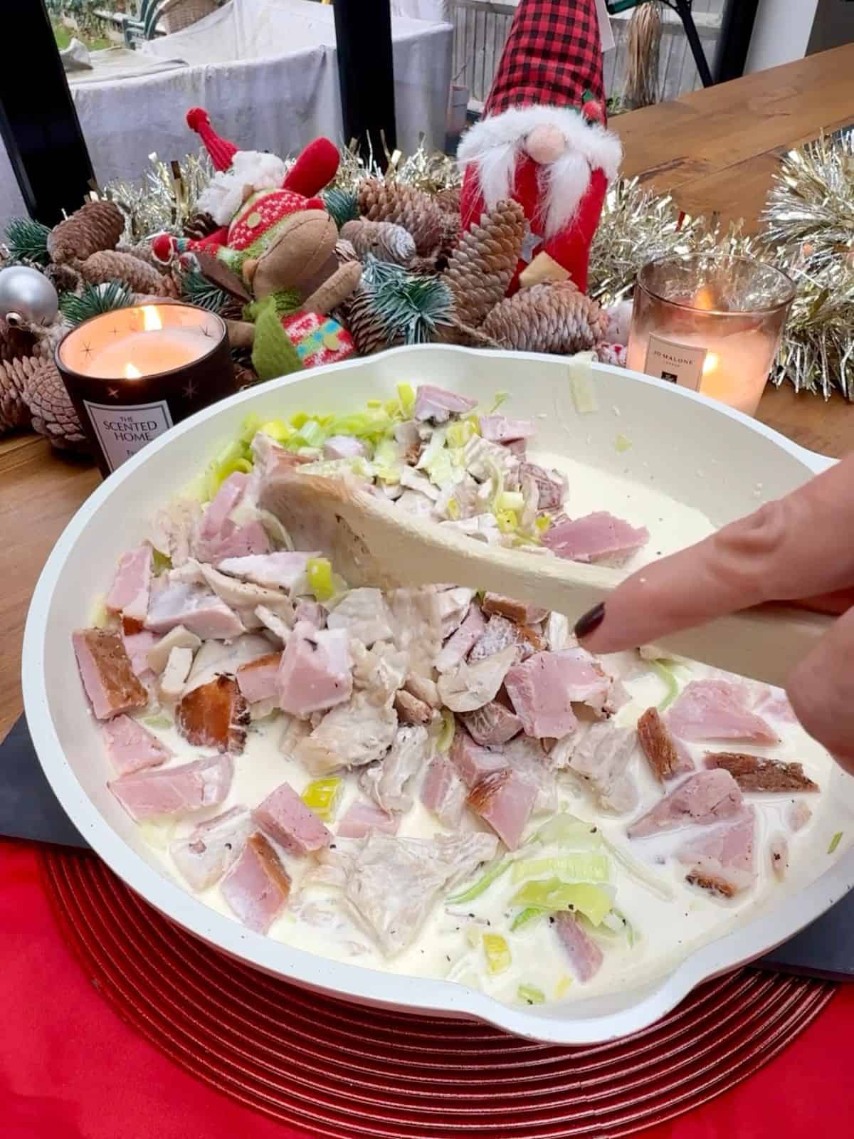 Chunks of turkey, ham and leek being stirred in a pan.