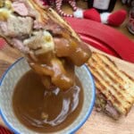 Christmas toasted sandwich being dipped into a pot of gravy.