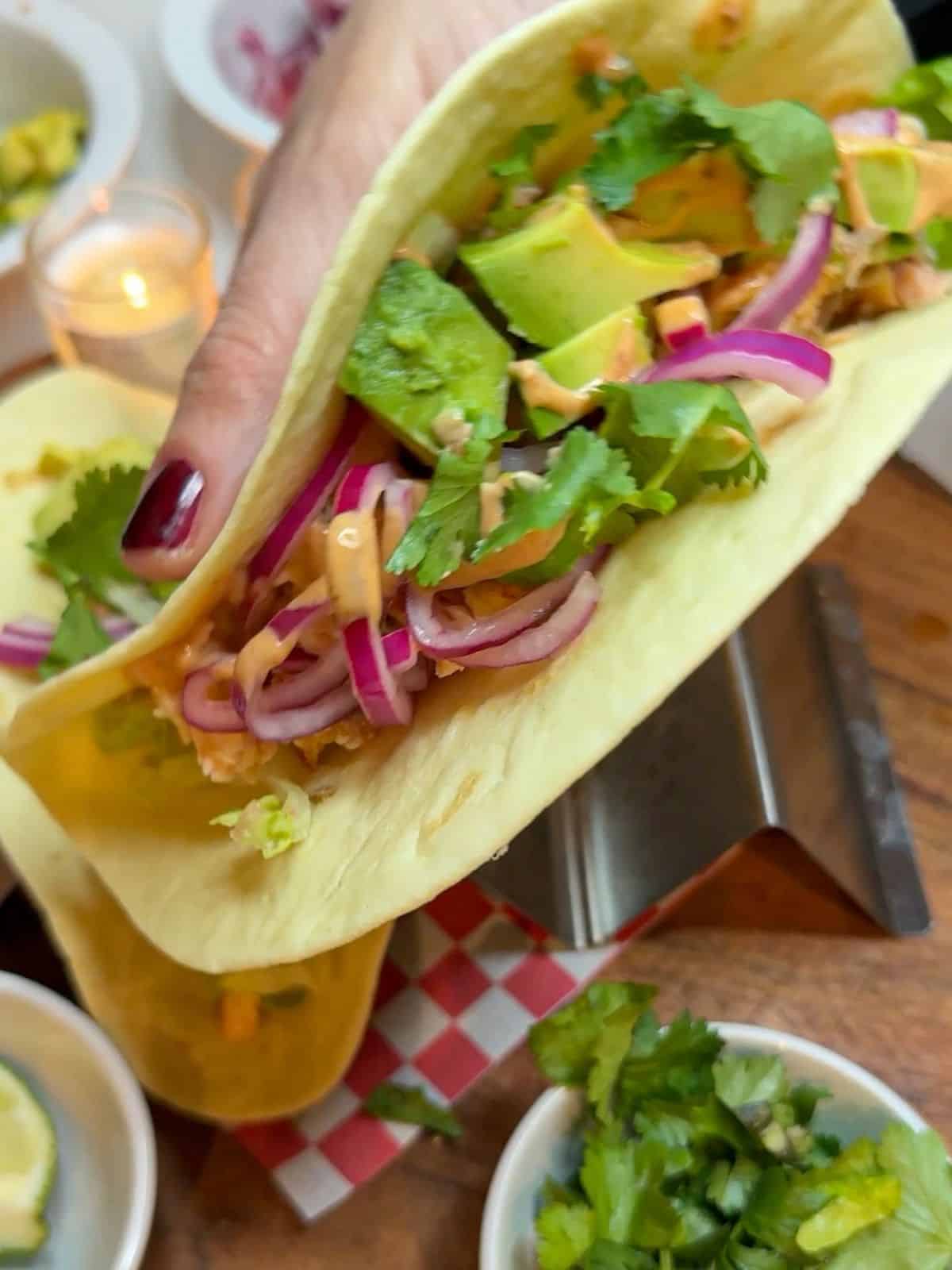 Someone holding a taco filled with salmon, red onion and avocado with chipotle sauce.