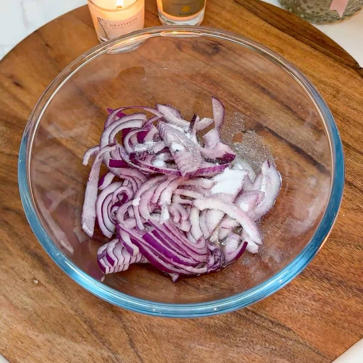 Red onion slices and sugar in a glass bowl.