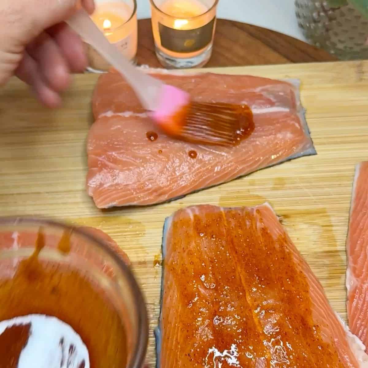 Salmon fillets on a chopping board being based with a glaze.