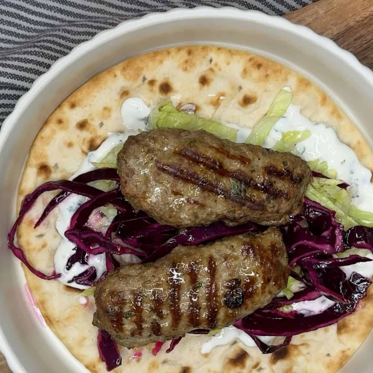Lamb kofta with red cabbage, lettuce and sauce on a flatbread.
