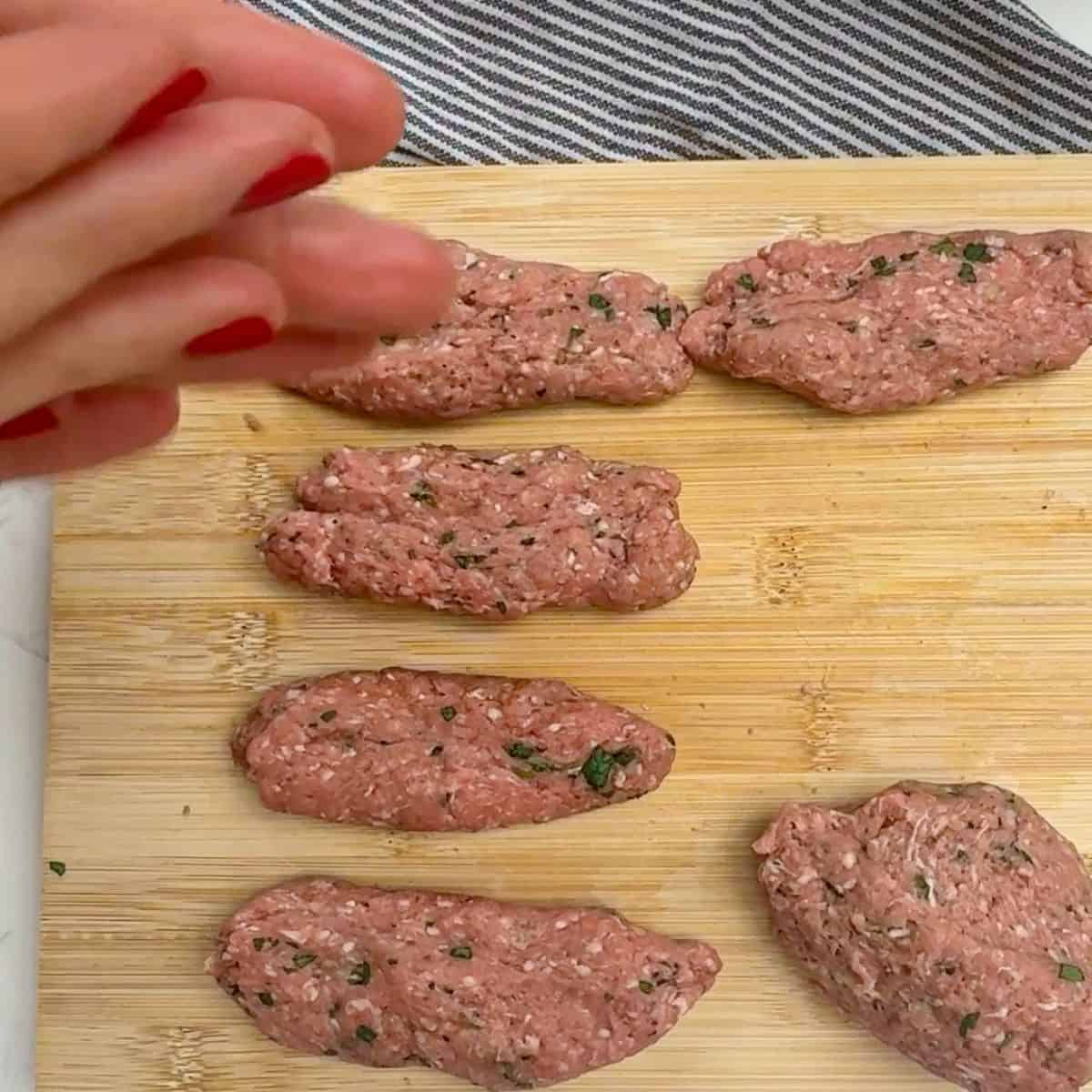 Raw lamb koftas on a chopping board.
