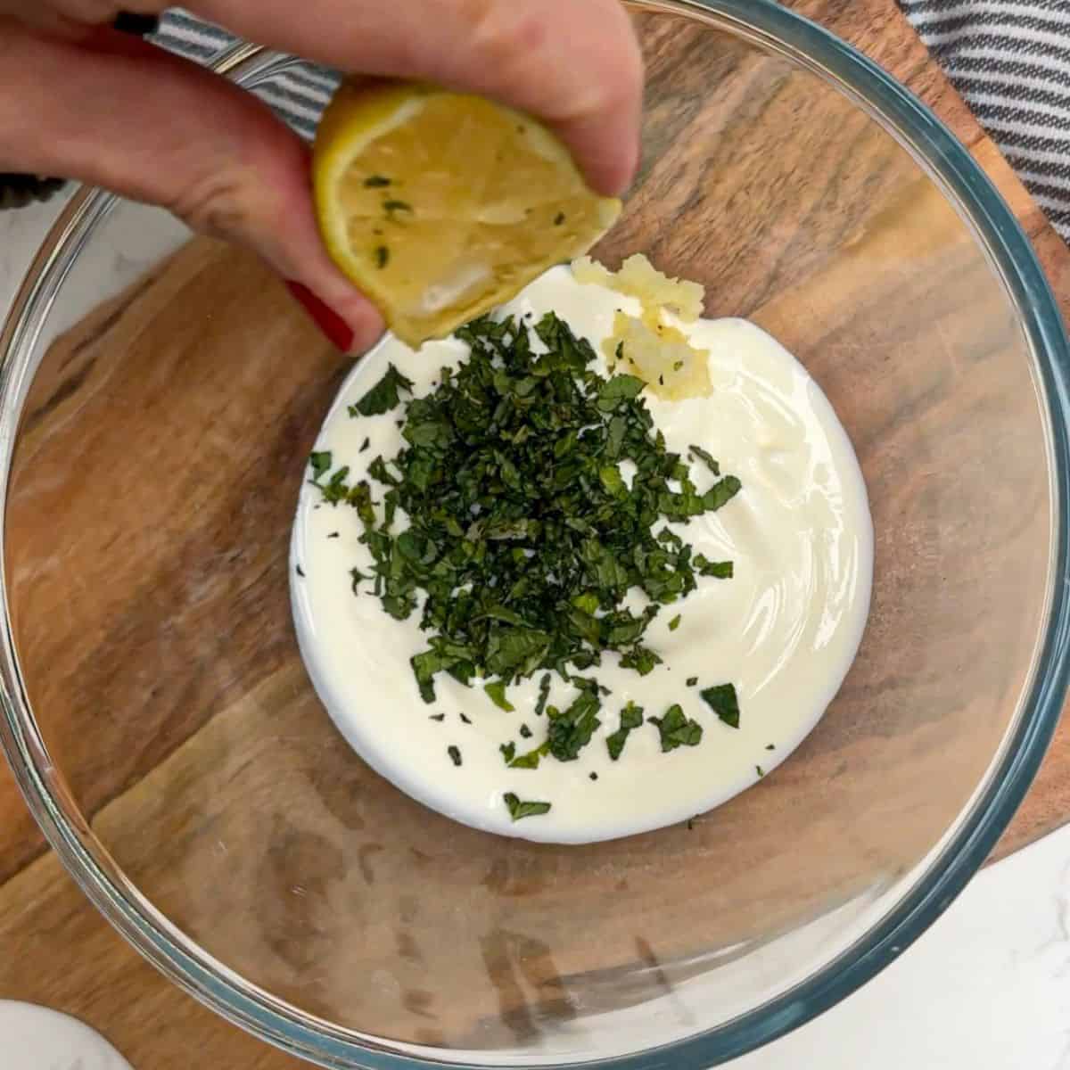 lemon being squeezed into a bowl of fresh mint and yoghurt.