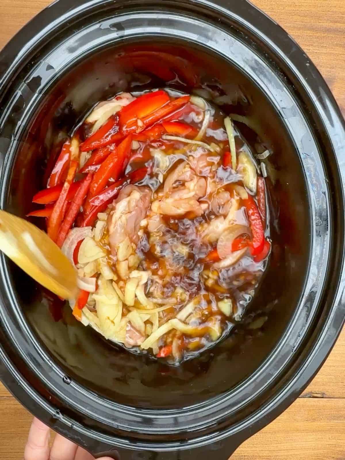 ingredients including red pepper being stirred in a slow cooker.