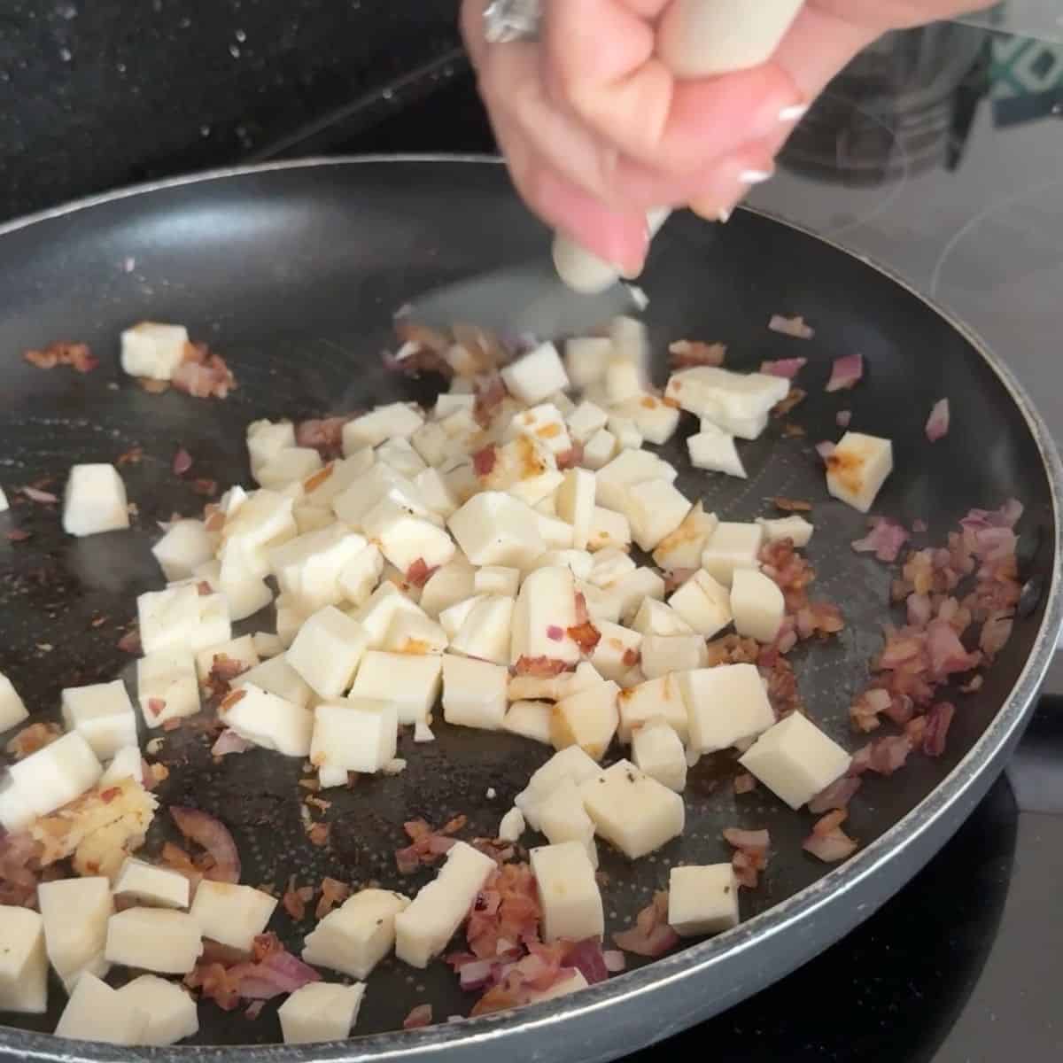 Halloumi & red onion being fried in a pan.
