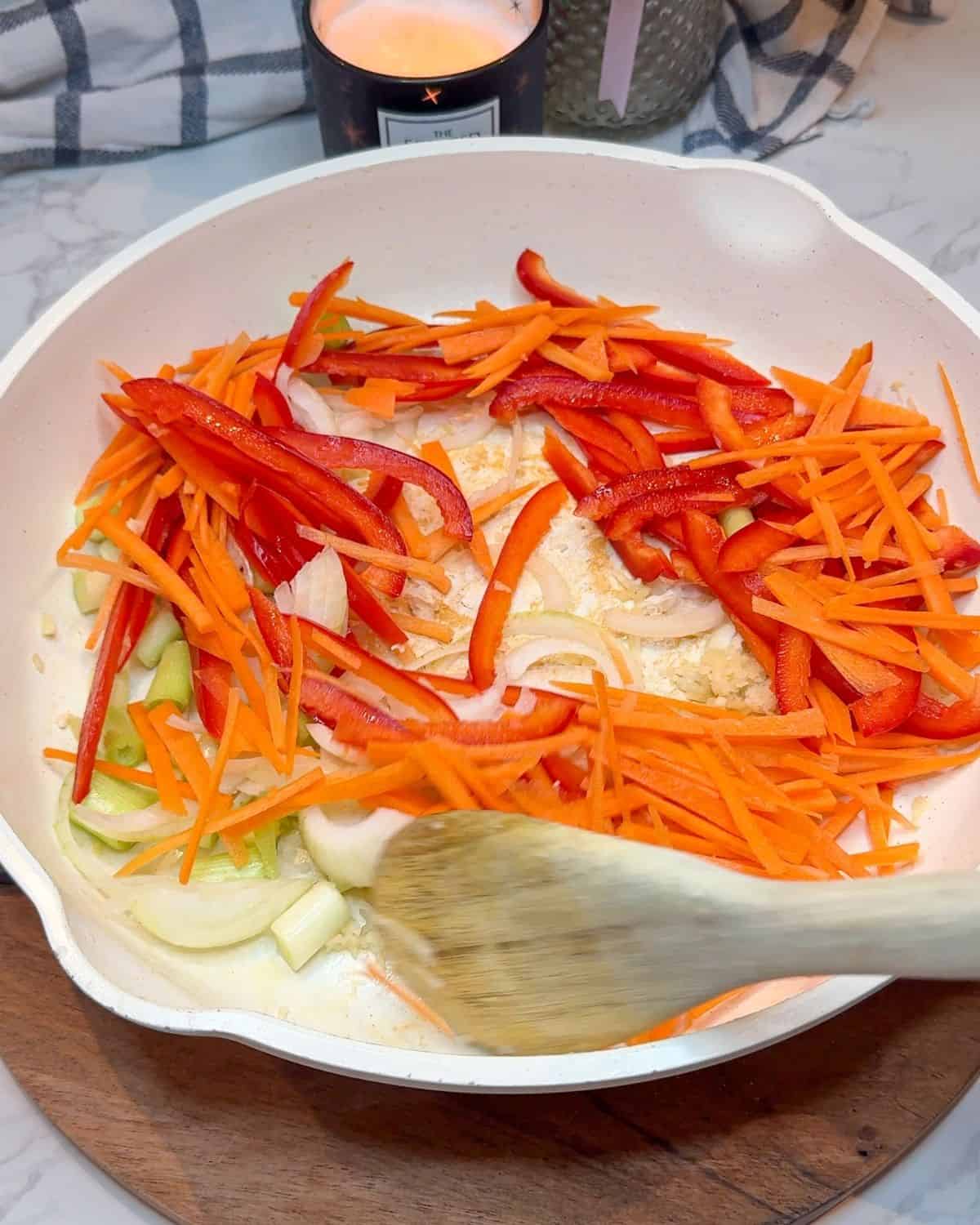 Sliced pepper, carrot & onion being cooked in a frying pan.
