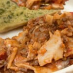 A plate of one pan lasagne with garlic bread in the background.