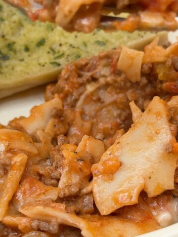 A plate of one pan lasagne with garlic bread in the background.