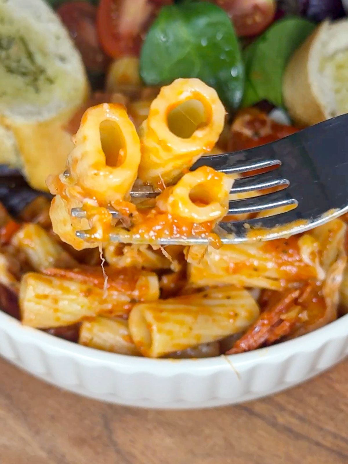 Rigatoni pasta on a fork and a bowl of pasta.