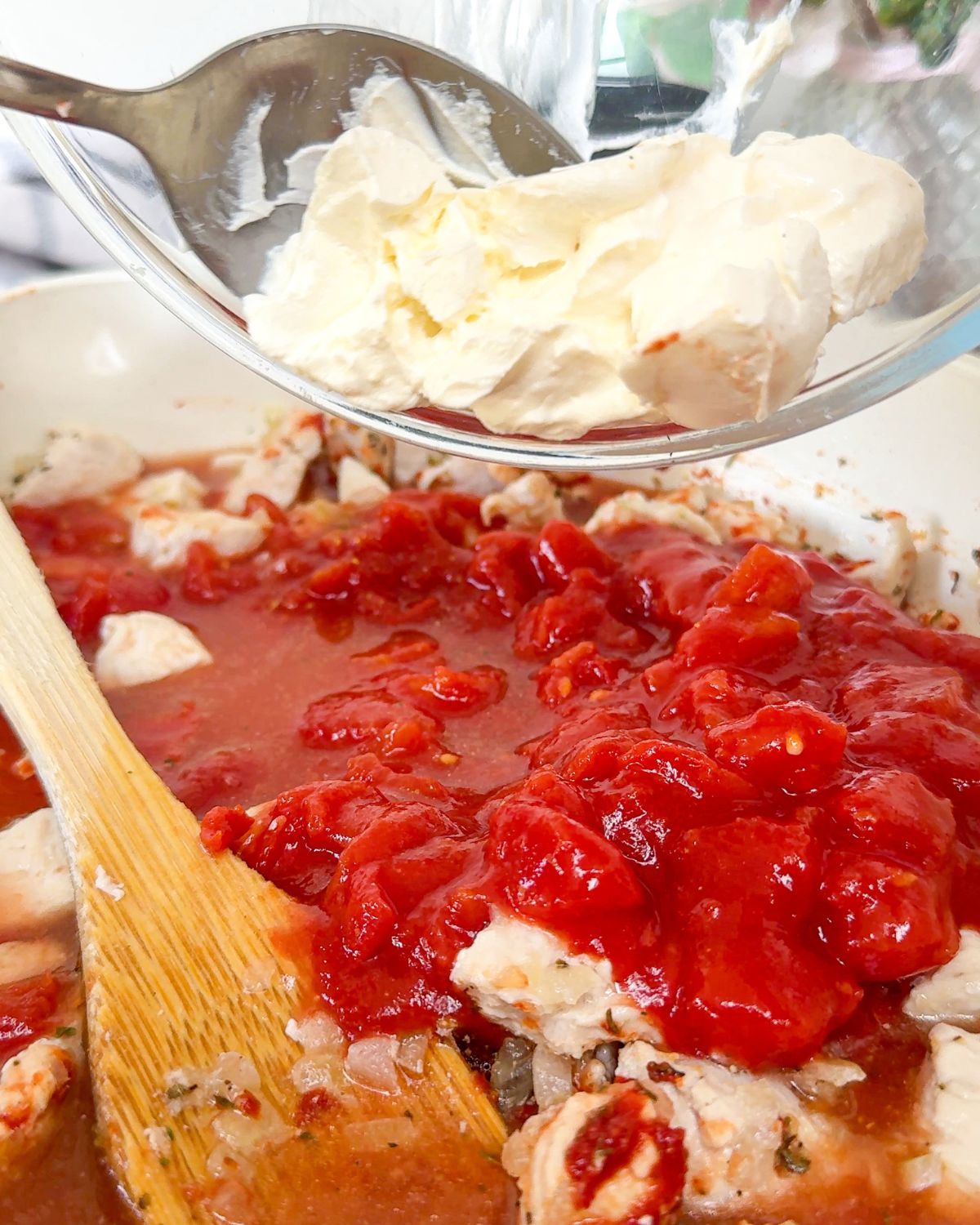 Cream cheese being poured into a pan containing chopped tomatoes & chicken.