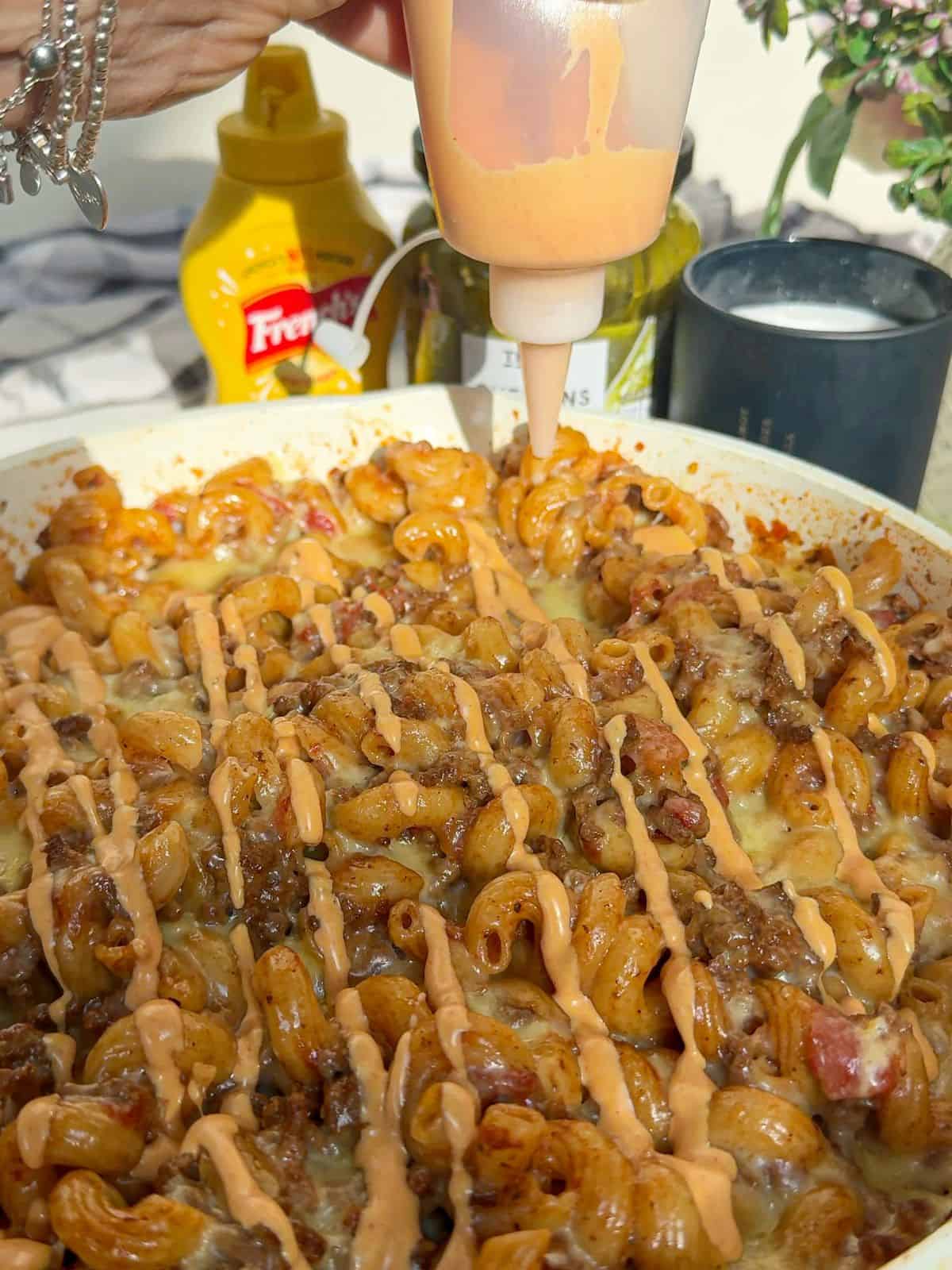 Burger sauce being drizzled over cheeseburger pasta.