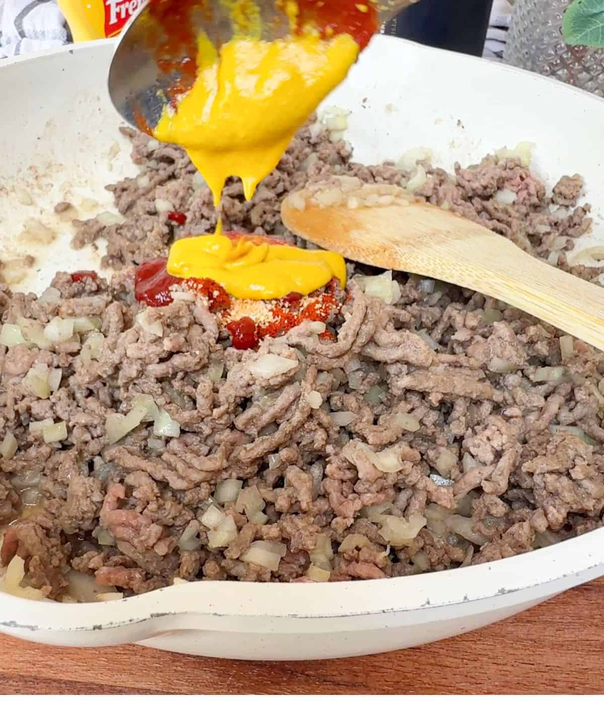American mustard being poured into a pan containing mince and onion.