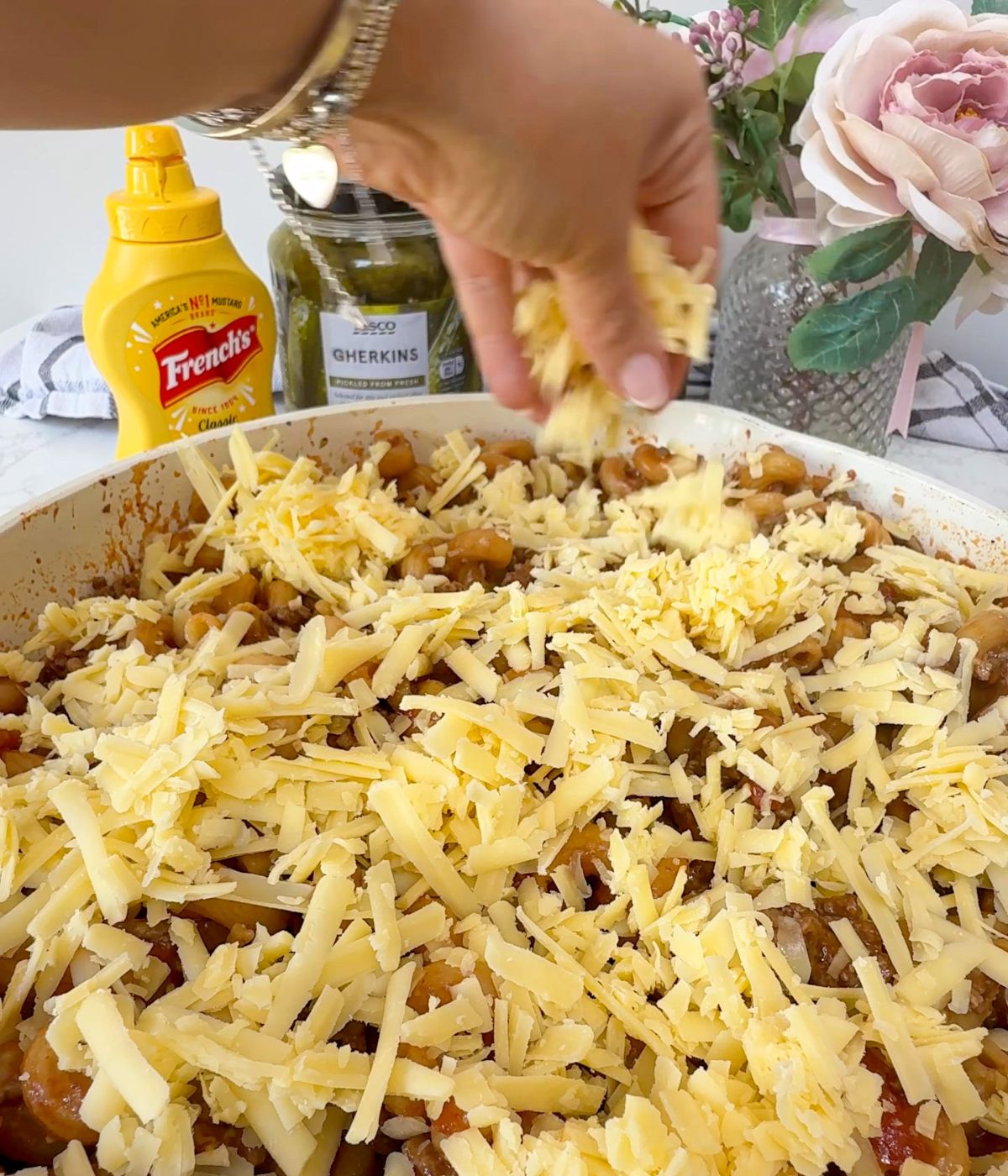 Grated cheese being sprinkled over pasta in a pan.